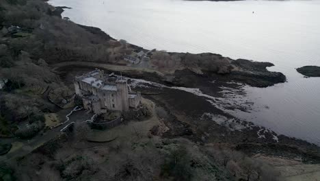 castillo de dunvegan en la isla de skye, rodeado de agua y bosque, cielo nublado, vista aérea