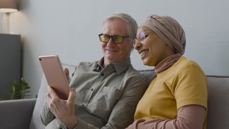 arabic woman and elderly man making a video call with a tablet while waving their hands 1