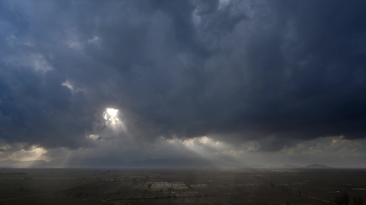 Dramatiske solstråler, der bryder igennem mørke stormskyer over et landligt landskab