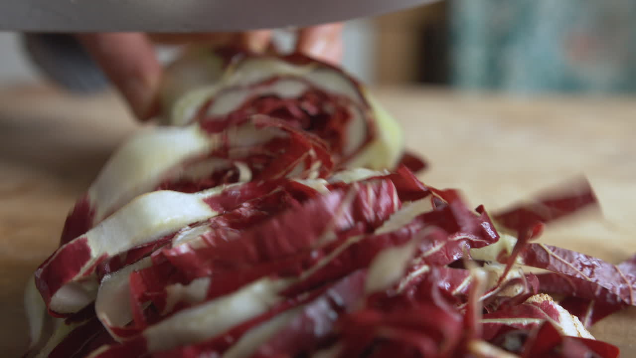 cerrar la mano de una mujer cortando hasta el final la achicoria italiana con un cuchillo afilado sobre una tabla de madera en su cocina