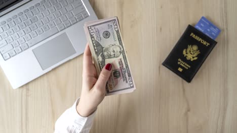 time lapse. woman hold banknote 50 u.s. dollars in hand and count it. american passport with boarding pass and laptop on the table. travel concept. cash. flat lay