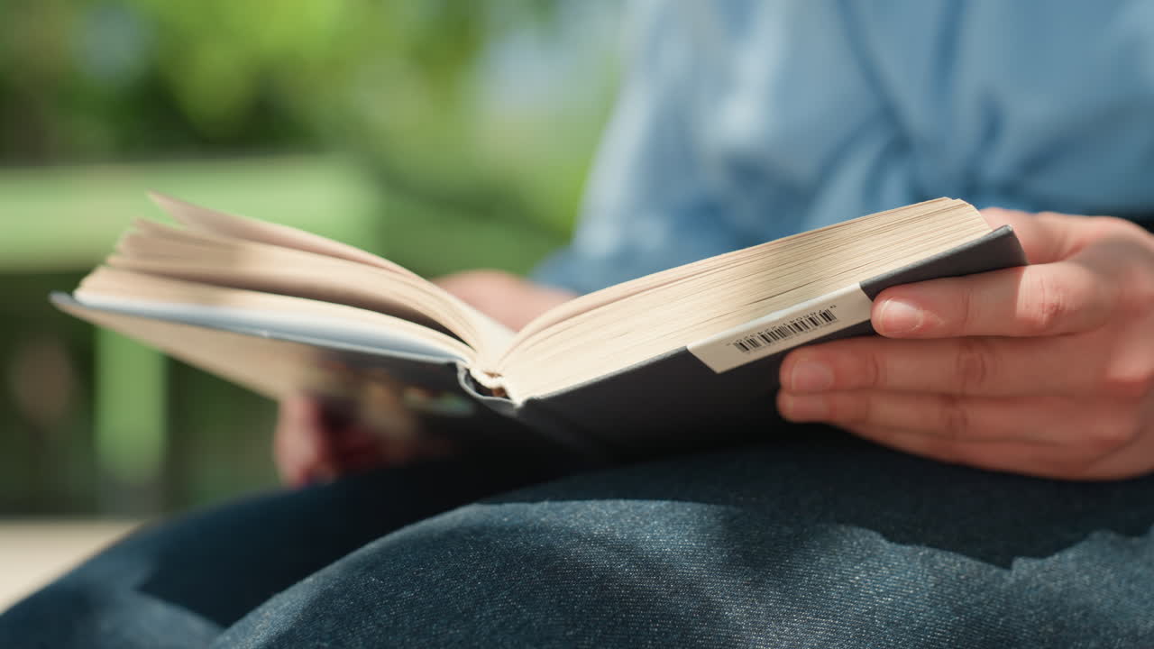 섬세한 백인 손이 페이지를 넘기는 모습 클로즈업, 편집자가 공원 벤치에서 원고 검토, 손가락으로 종이 질감을 따라 그림, 페이지가 넘어가는 슬로우 모션, 부드러운 햇빛과 흐릿한 녹색 배경
