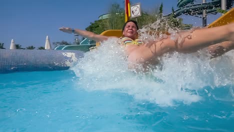 descenso del tobogán acuático en un parque acuático de vacaciones. cámara lenta en un tobogán acuático vacaciones familiares, una mujer en bikini desciende del tobogán en una piscina de agua azul salpicando gotas de agua.