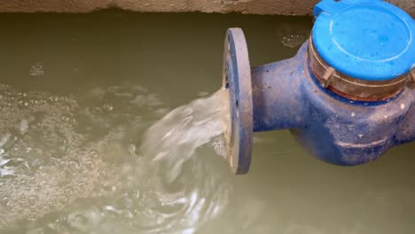 close-up of waste water flowing from a blue industrial pipe into waste water treatment pond