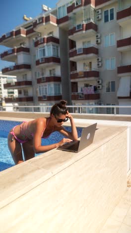 woman working on a laptop by a rooftop pool