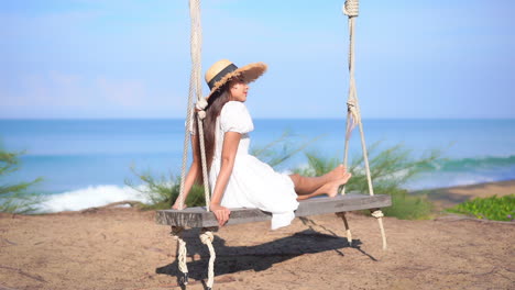 Mujer-Exótica-Con-Vestido-Blanco-De-Verano-En-Un-Columpio-De-Madera-Junto-A-Una-Playa-Tropical-En-Un-Día-Soleado,-Fotograma-Completo