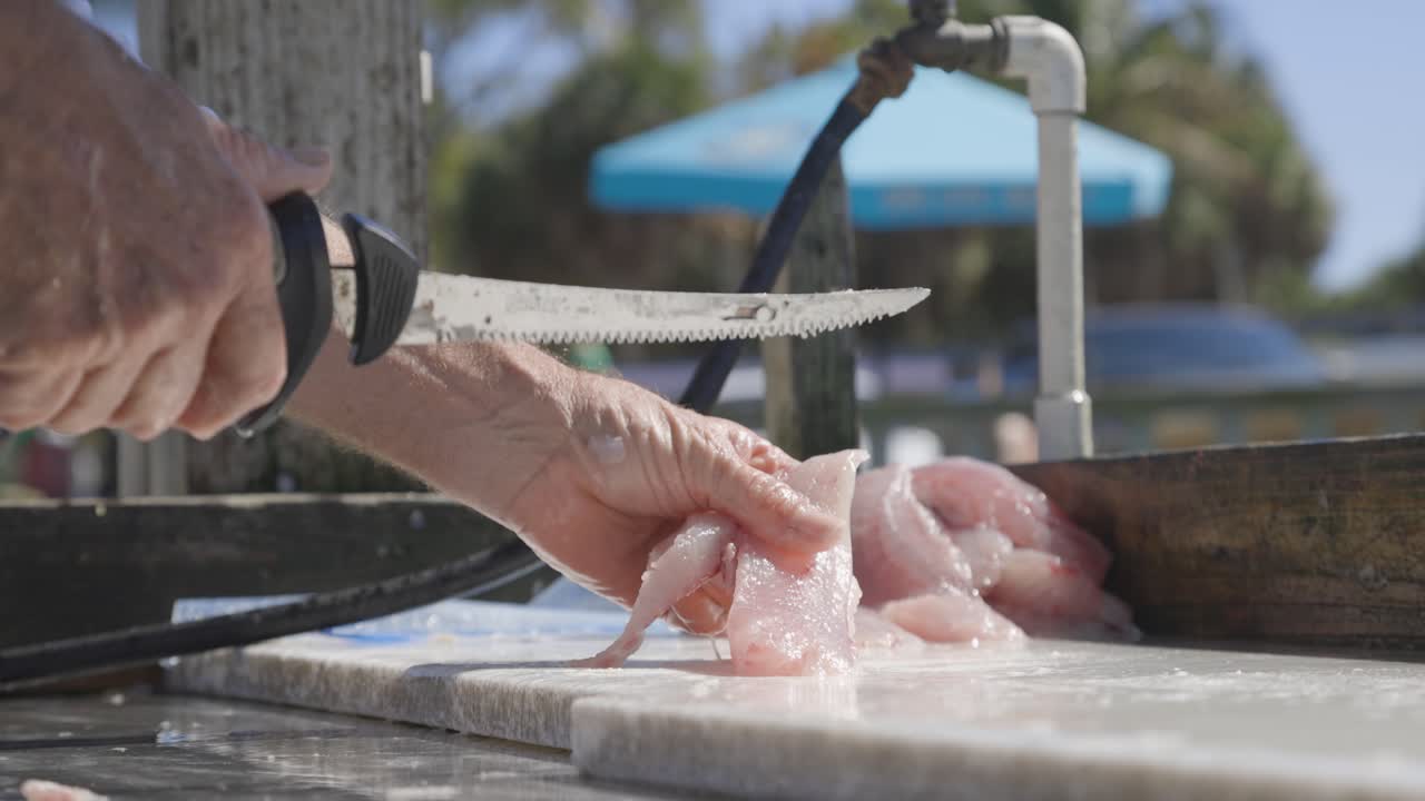 hombre cortando carne de pescado en la mesa de limpieza en un muelle cerca de su barco en florida