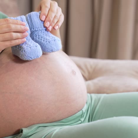 tummy of a pregnant woman where she puts cute newborn socks and walks with them. expecting mother playing with little baby socks on her tummy