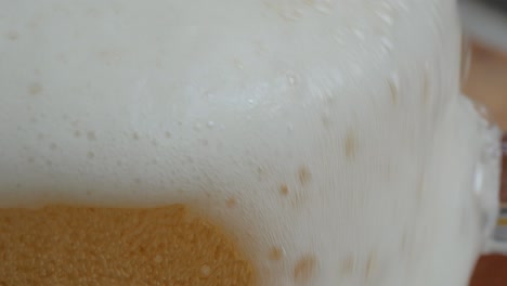 the tip of a crystal beer glass in focus as the beer is being poured, and the frothy foam fills the glass full