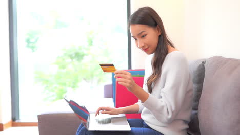 Homestay-Mujer-Asiática-Comprando-En-Línea-Con-Computadora-Portátil-Y-Tarjeta-De-Crédito,-Fotograma-Completo-En-Cámara-Lenta