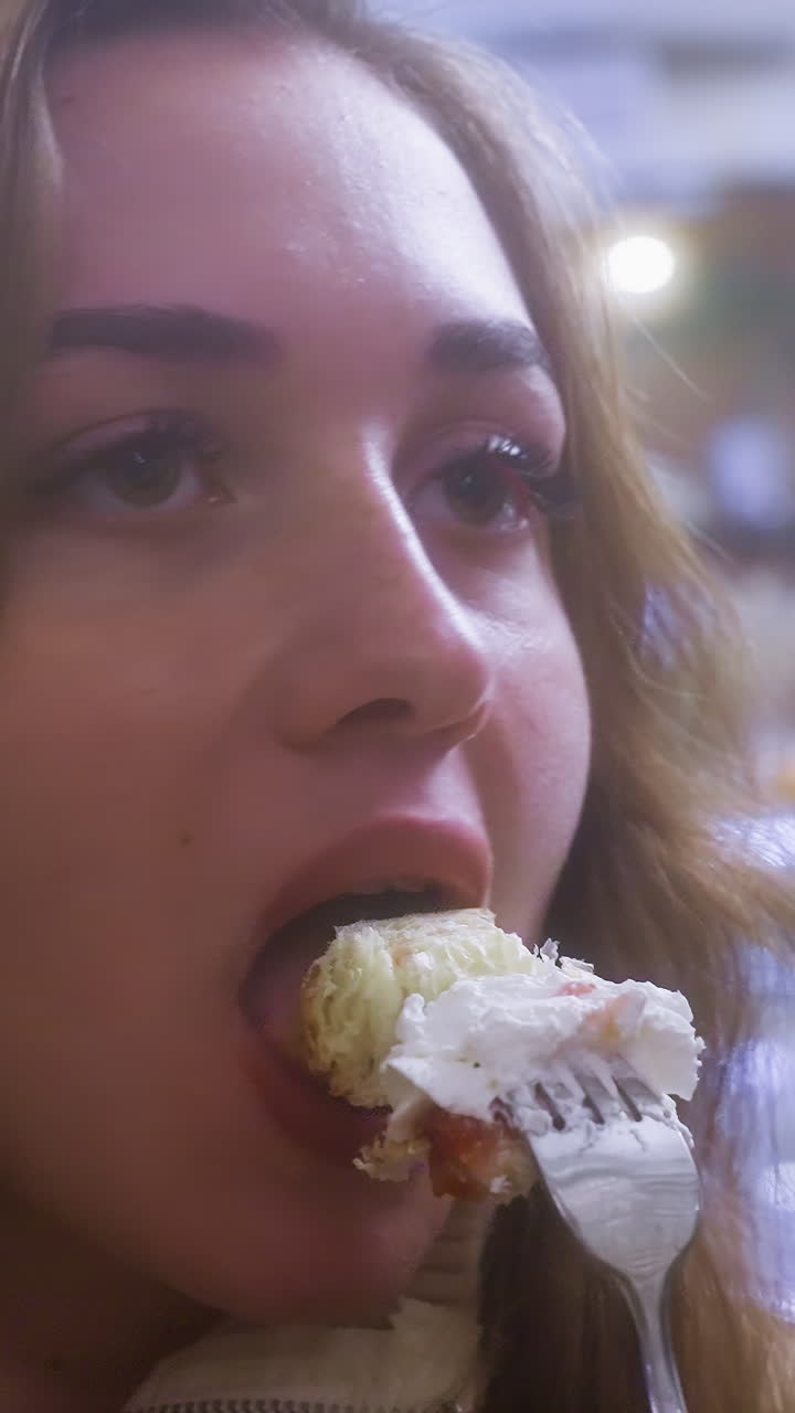 Close-up of young woman eating creamy croissant with fork in cozy cafe, enjoying dessert. Whipped cream and fruit topping visible, highlighting the indulgent, relaxed atmosphere