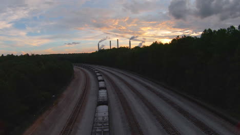 fpv flight over rail road tracks and forest with power plant in distance during golden hour