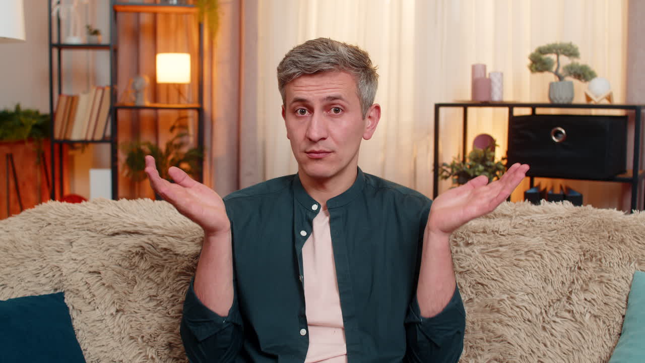 Young man lifts hands in air and looks confused reacting to unexpected situation or sudden question