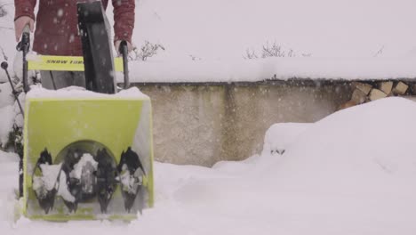 filmed from the front, watch as a person operates a yellow snowblower to clear a snowy driveway in slow motion