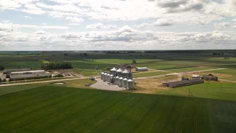 Vista-Por-Drones-De-Silos-Agrícolas,-Plantas-De-Fabricación-De-Graneros,-Almacenamiento-De-Productos-Agrícolas-Y-Elevadores-De-Granos-En-Medio-De-Un-Campo-Cultivado-Verde,-Acercar