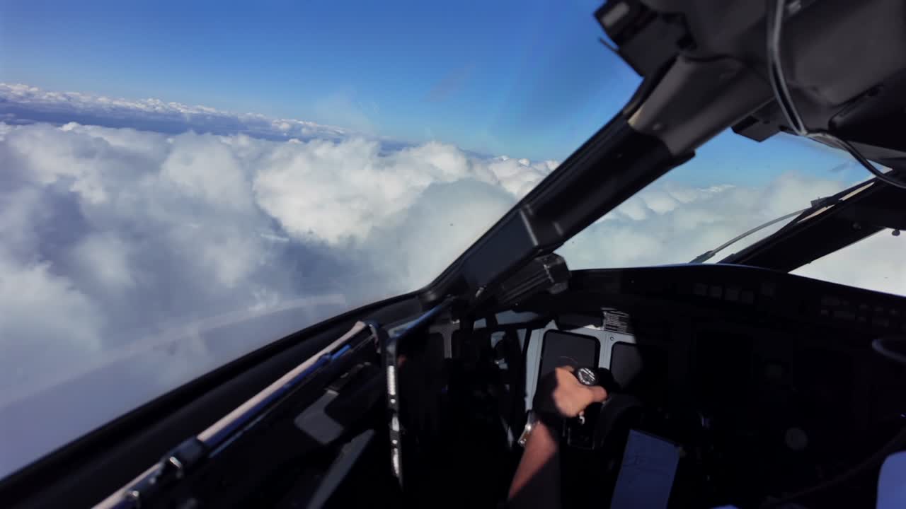 An immersive pilot’s view from inside a jet airplane cockpit while flying manually over an endless layer of cottony storm clouds, under a blue sky. Captain is handling the flight controls.
