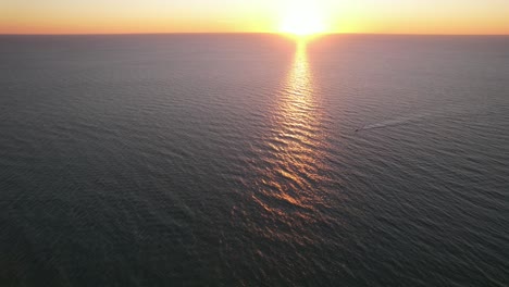 drone clip over open sea at beautiful orange sunset, moving towards a boat moving right to left leaving ripples across the water