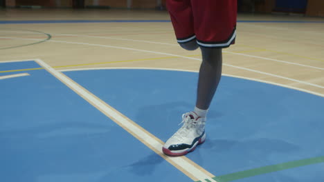 basketball athlete stretches his legs in the middle of an empty court, engaging in a pre-game routine to limber up and prepare for his upcoming match