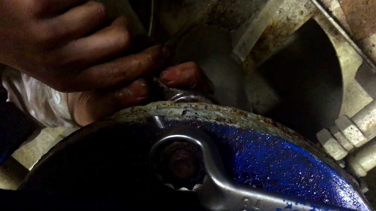 Primo piano delle mani di un uomo che stringono un grande bullone su un macchinario all'interno di una barca