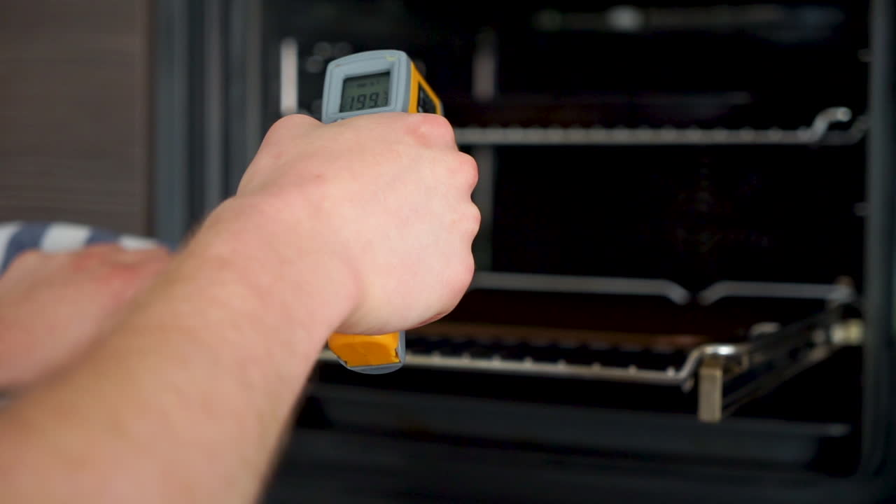 Young aspiring chef is checking the temperature of a pizza, bread steel in the oven with a infrared thermometer.