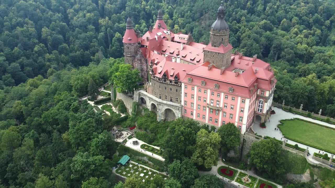 Aerial establishing orbit of Ksiaz Castle, Poland, historic palace on hill with red orange tinted roof and grand lawn