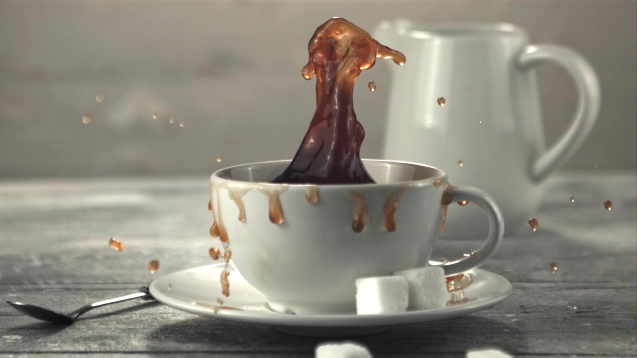 Zeitlupenaufnahme: Zuckerwürfel fällt in eine Kaffeetasse.
