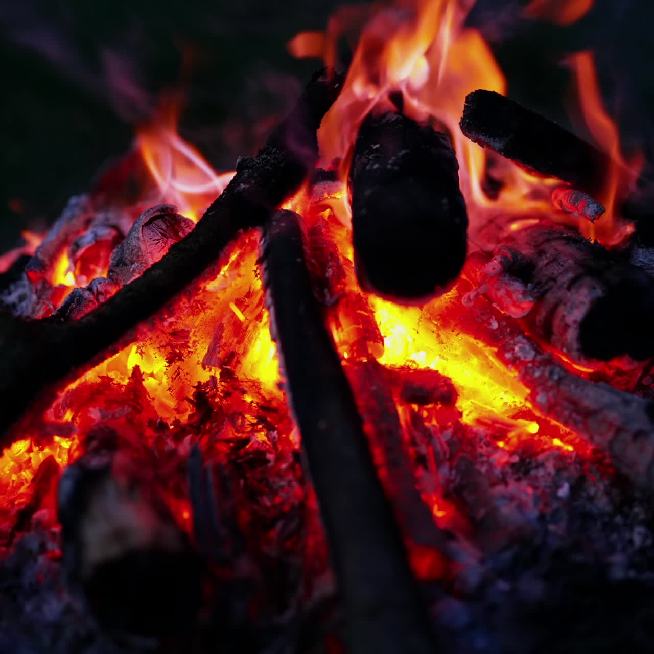 Beautiful bonfire on dark background. Red and yellow flame with smoldering logs at night. Romantic campfire in summer evening. Close-up