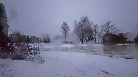 Fondo-De-Invierno-Timelapse-Con-Gotas-De-Lluvia-Sobre-Lentes-A-Través-De-Un-Lago-Congelado-Y-Un-Granero-En-El-Campo-De-Letonia