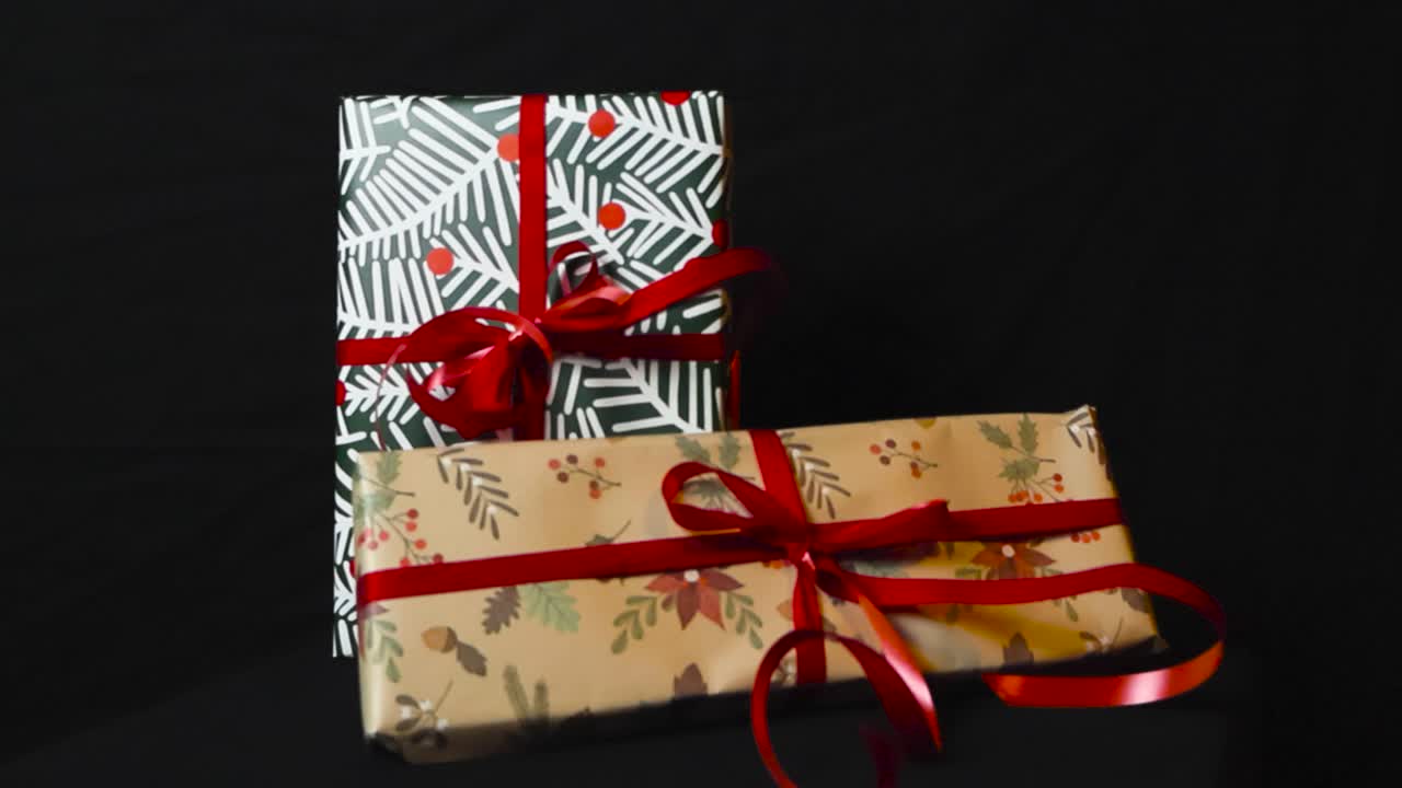 filmagem cinematográfica de close-up de presentes de natal em papel de embrulho colorido e fitas vermelhas em um fundo preto, enquanto a filmagem lentamente se afasta deles. o embrulho é branco, verde-marrom, com textura