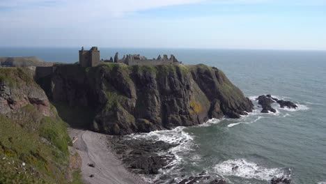 Impresionante-Vista-De-Gran-Angular-De-Los-Magníficos-Acantilados-Sobre-Los-Que-Descansa-El-Castillo-De-Dunnottar,-Con-Olas-Rompiendo-En-El-Océano-Y-Gráciles-Pájaros-Volando-Por