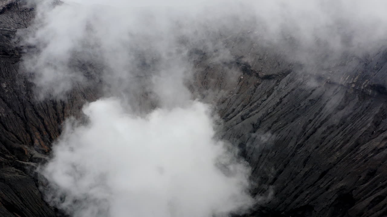 Man running on peak of Volcano, Aerial push revealing active Mt Bromo