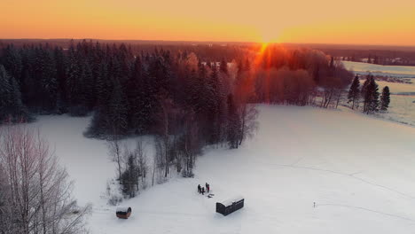 amazing aerial yellow and orange sunset over a winter forest landscape with an unrecognizable family enjoying the snow