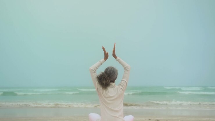Rear view of active senior African American woman doing yoga on exercise mat at the beach 4k