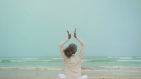 rear view of active senior african american woman doing yoga on exercise mat at the beach 4k