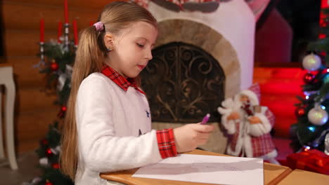 little girl drawing or writing letter for santa at christmas decorated room. cute child sitting on floor and creating picture on small desks. christmas mood concept