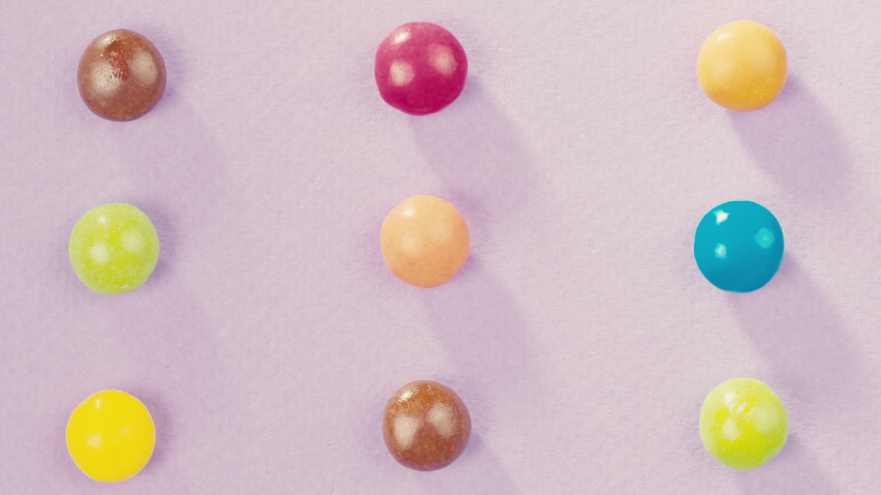 Colorful dragee candies with glitter sprinkles on purple background. Summer bright studio shot for store, supermarket, close up top view, zoom. Children sweets made of sugar, mix of lollipops.