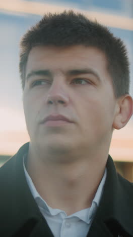 hombre de traje negro ajustando el cuello con una expresión enfocada al aire libre, el fondo destaca edificios modernos de vidrio y estructuras urbanas