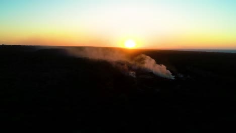 el humo se eleva a través del paisaje oscuro y estéril mientras el sol se sumerge bajo el horizonte.