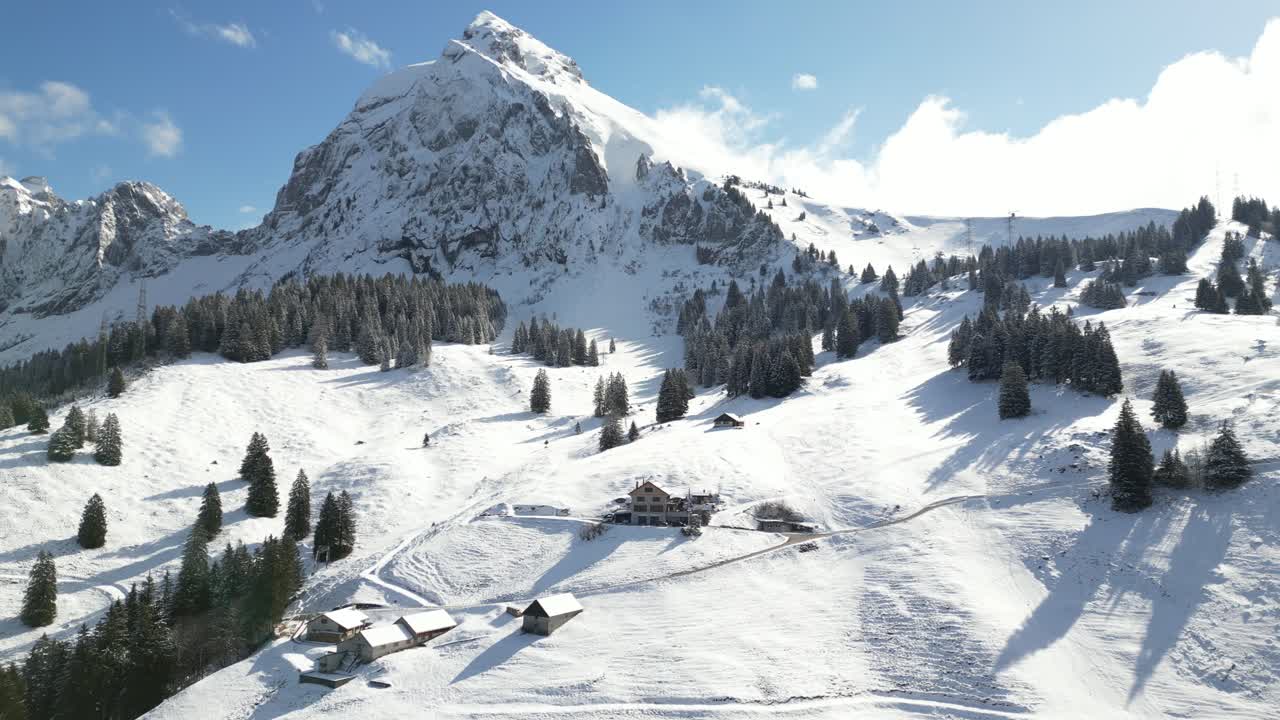 panorámica aérea disparada sobre las casas de la aldea a lo largo de la ladera de la montaña cubierta de nieve blanca sobre fronalpstock, suiza glarus durante el día