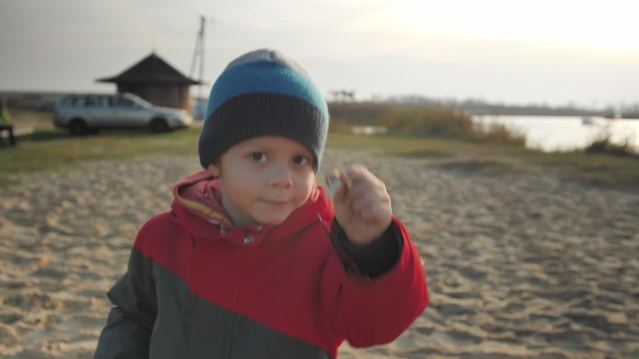 Iloinen poika tanssii ja näyttää tyhjää etanankuorta järven rannalla.