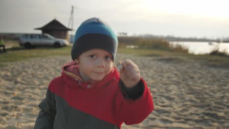 happy boy dances and shows an empty snail shell by the lake