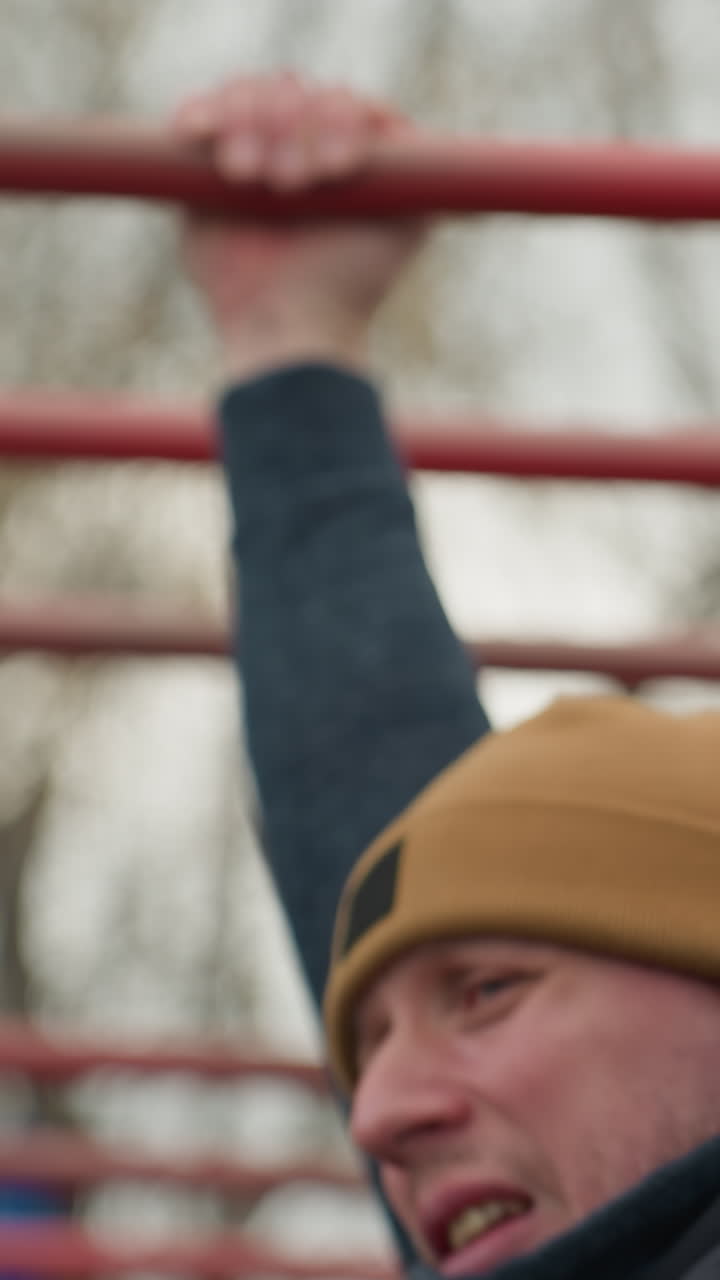 Close-up of a coach exerting effort as he navigates across red iron bars, with a blurred background of bare trees