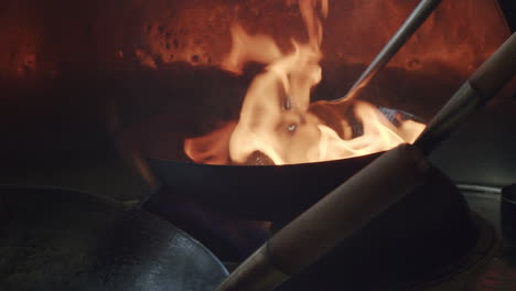 fire strikes in a wok pan. a spatula moves around. the footage is in slow motion.