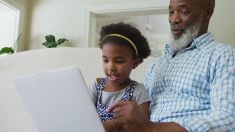 Feliz-Abuelo-Afroamericano-Con-Nieta-Usando-Tableta-En-La-Sala-De-Estar