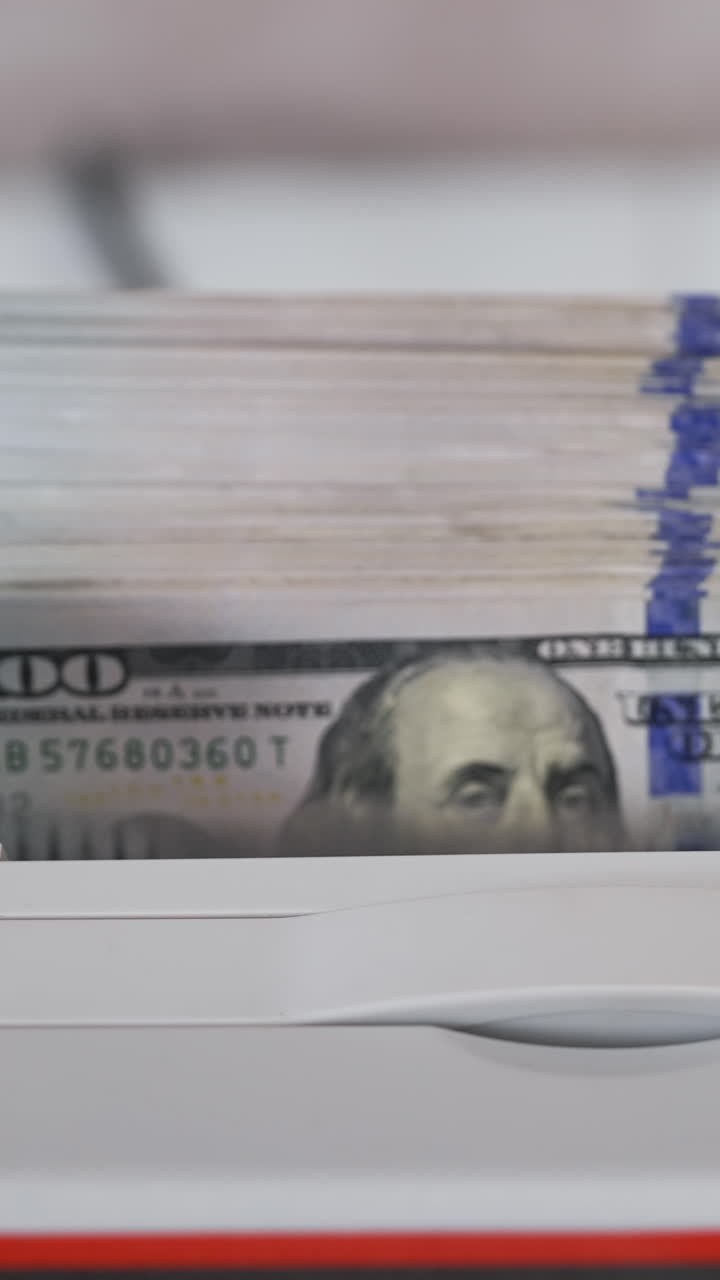 Electronic equipment for counting paper money. Bank worker putting a bundle of one hundred dollar bills into the counting machine for calculation. Vertical video