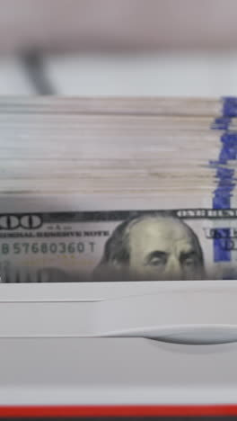 electronic equipment for counting paper money. bank worker putting a bundle of one hundred dollar bills into the counting machine for calculation. vertical video