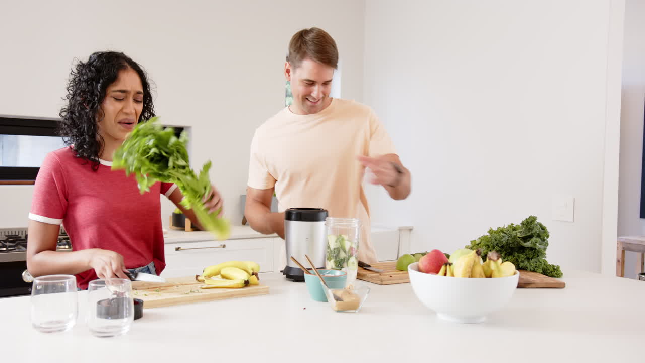 Preparing healthy smoothie, young multiracial couple chopping fruits and vegetables, at home