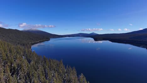 wide drone shot above snowy trees and clear lake on sunny winter day, 60fps