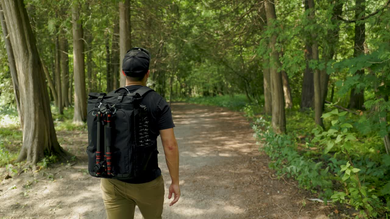 현대적인 카메라 백팩과 삼각대 장비로 울창한 녹색 숲을 하이킹하는 사진작가