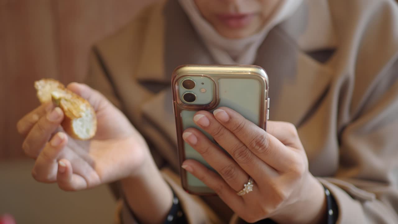 Primo piano di donna che mangia pane mentre usa lo smartphone